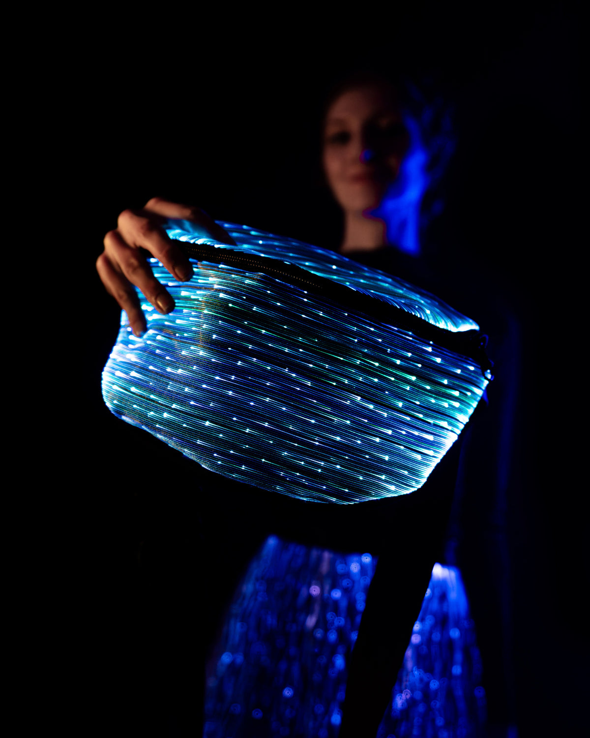 NEBULITE Fanny Pack 4 in Classic fabric held up in one hand, the straight parallel fibres lit blue and teal